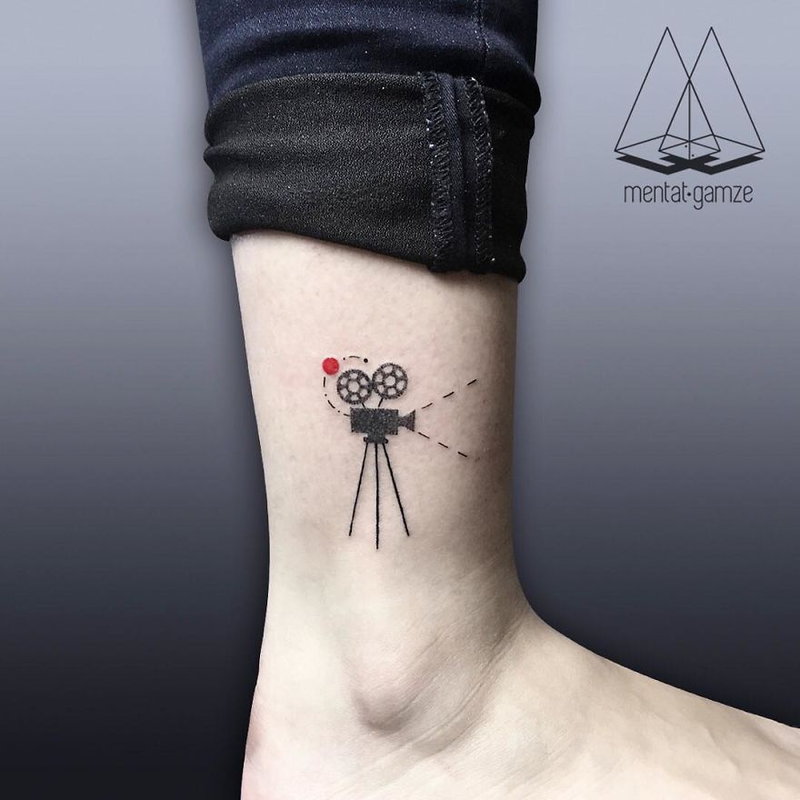 Minimalist tattoo of a camera with a red dot on an ankle, showcasing tattoo artist's unique style.
