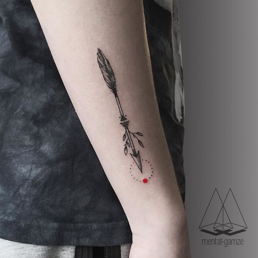 Tattoo of an arrow on an arm, featuring a small red dot at the tip, showcasing tattoo artist's work.