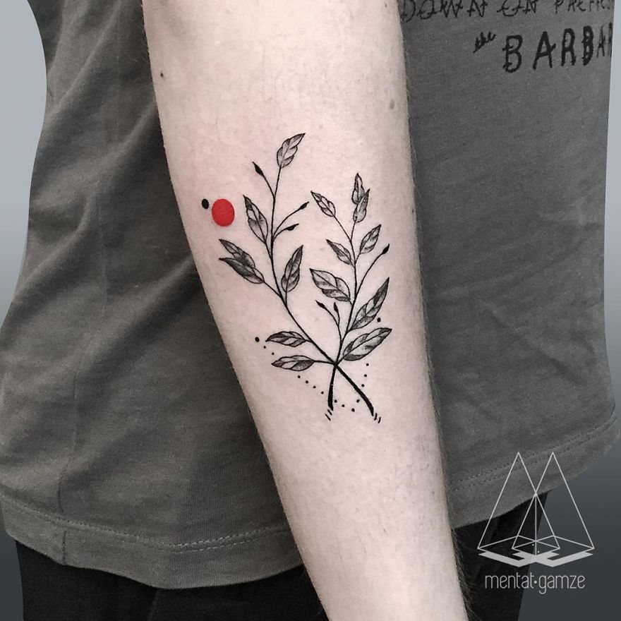 Forearm tattoo featuring a black leaf design with a striking red dot, showcasing tattoo artistry.
