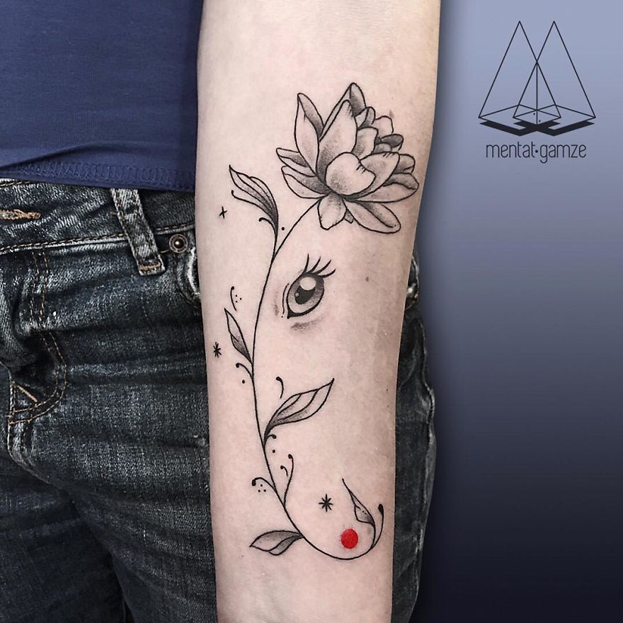 Tattoo featuring a floral design with an eye and a red dot on an arm, representing a tattoo artist's creativity.