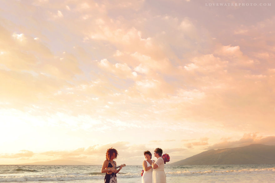 Two woman holding hands in a beach near a pastor 