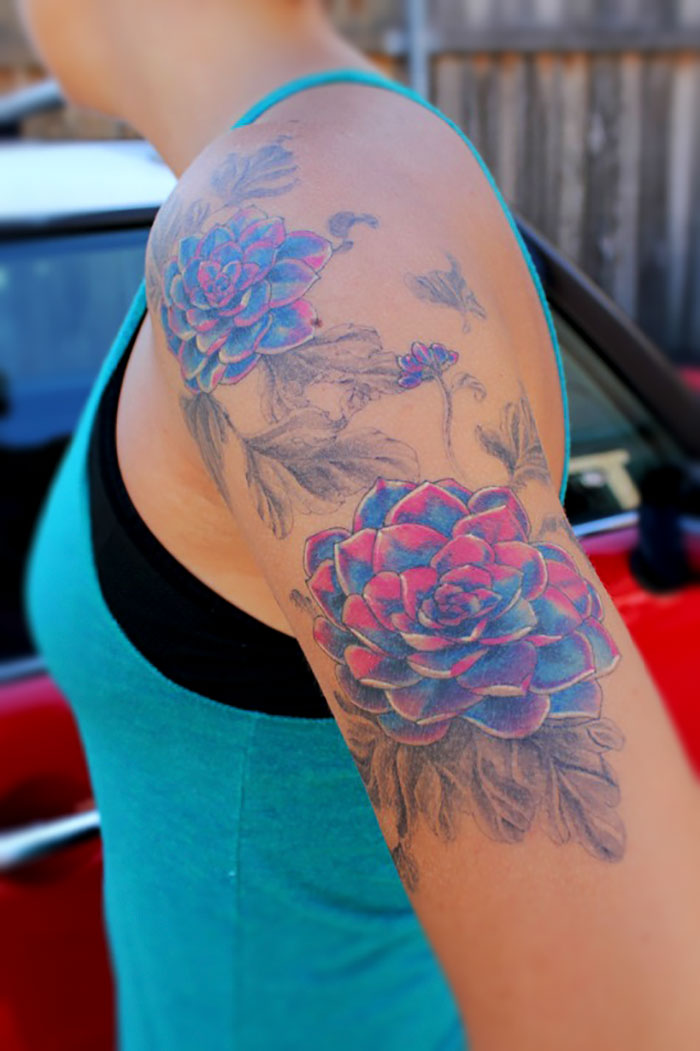 Colorful succulent tattoo on a person's upper arm with floral details.