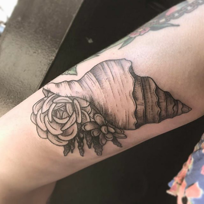 Succulent tattoo design featuring a detailed shell with flowers on an arm.