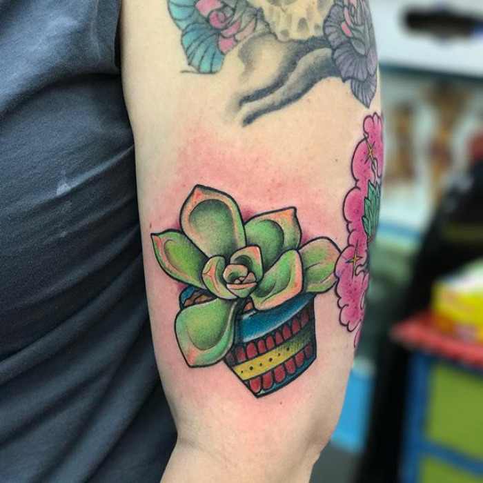 Colorful succulent tattoo on upper arm with decorative pot design.