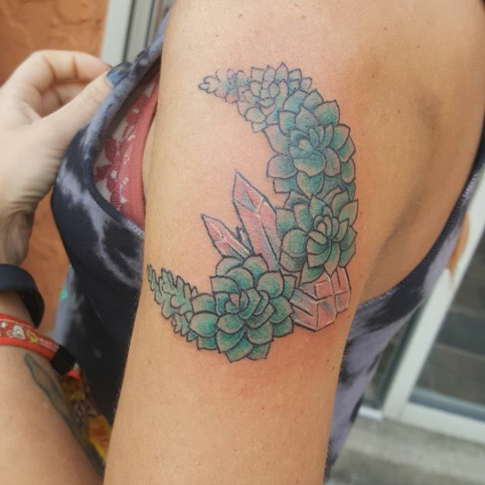 Succulent tattoo featuring green plants and crystals on a person's upper arm.
