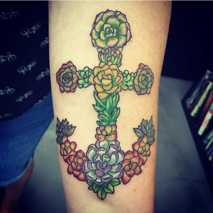 Succulent tattoo art featuring colorful plants arranged in a cross shape on a forearm.
