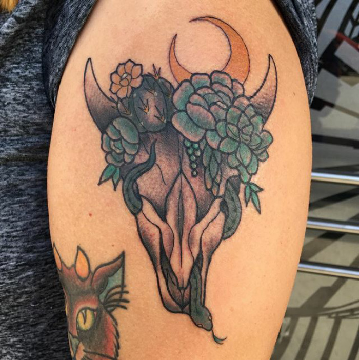 Arm tattoo of a bull skull adorned with colorful succulent designs and a crescent moon.