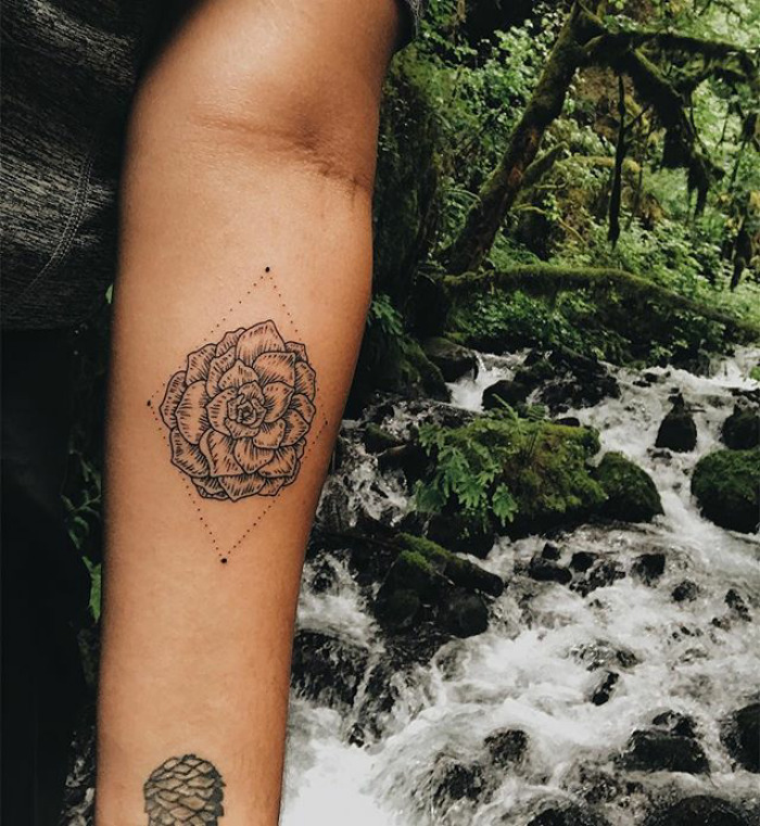 Succulent tattoo design on a person's forearm in a lush forest setting near a cascading stream.