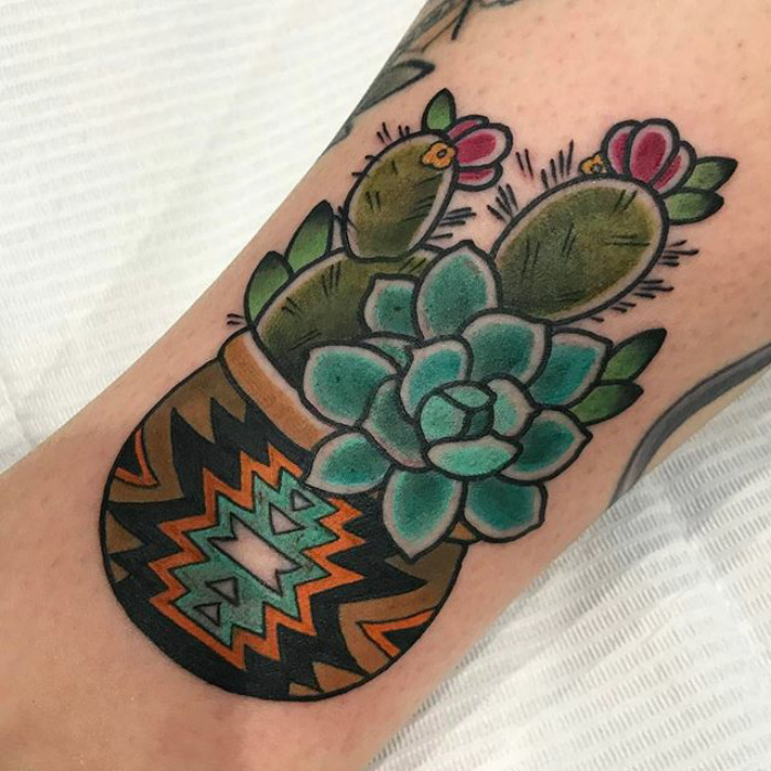 Colorful succulent tattoo in a patterned pot on forearm, featuring cacti with flowers.