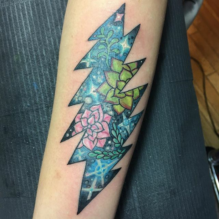 Colorful succulent tattoo in a zigzag pattern on forearm, featuring pink and green succulents against a starry background.