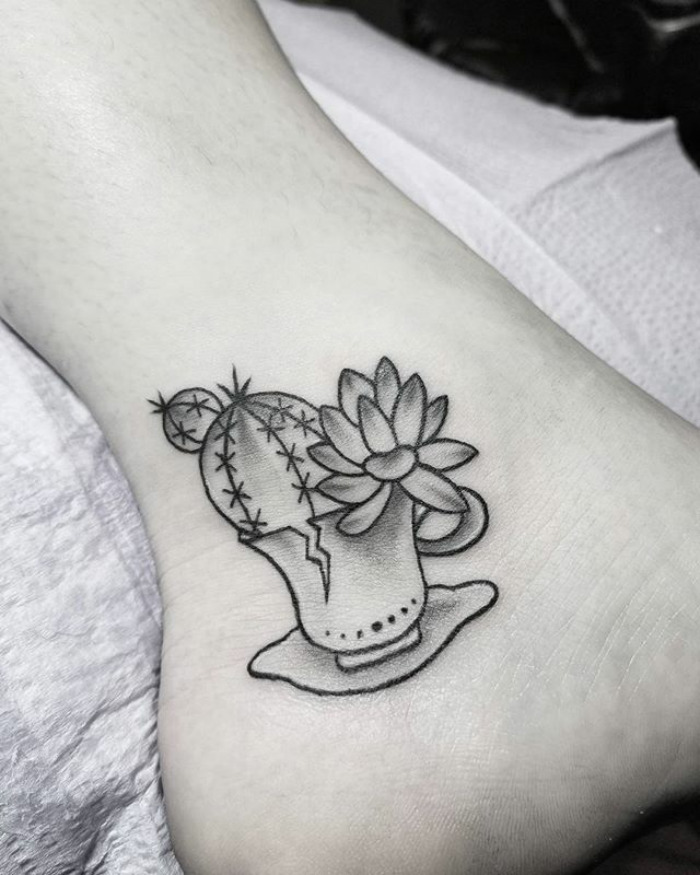 Black and grey succulent tattoo of a potted cactus and flower on the ankle.
