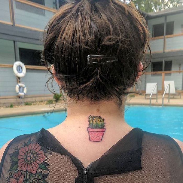 Back view of a person by a pool, showcasing a small succulent tattoo on their neck.
