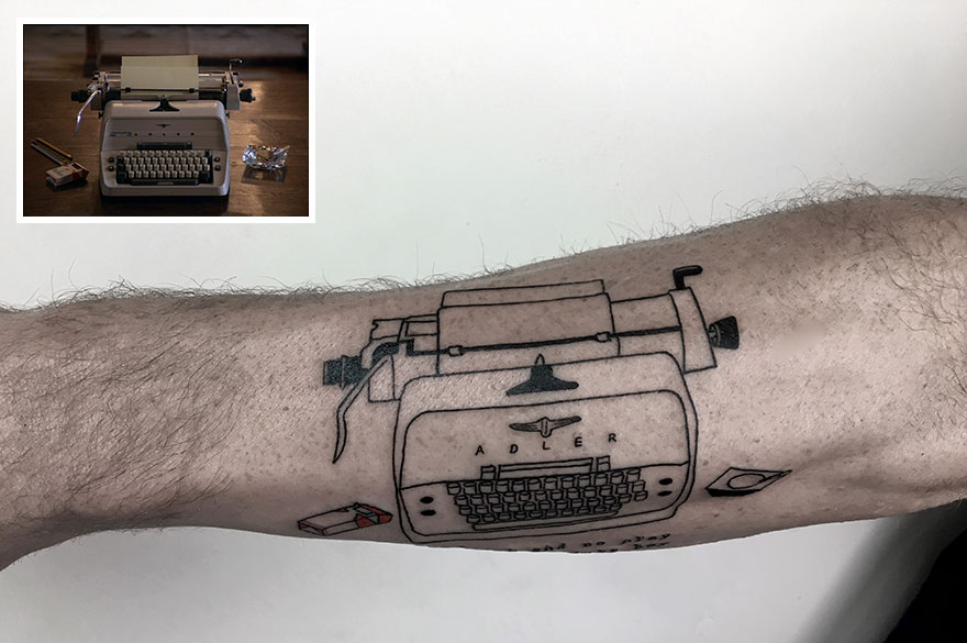 Tattoo of a typewriter on an arm, modeled after a real Adler typewriter in the background.