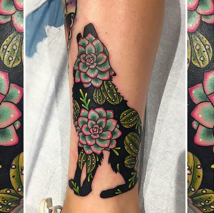 Wolf silhouette tattoo filled with colorful succulent designs on leg.
