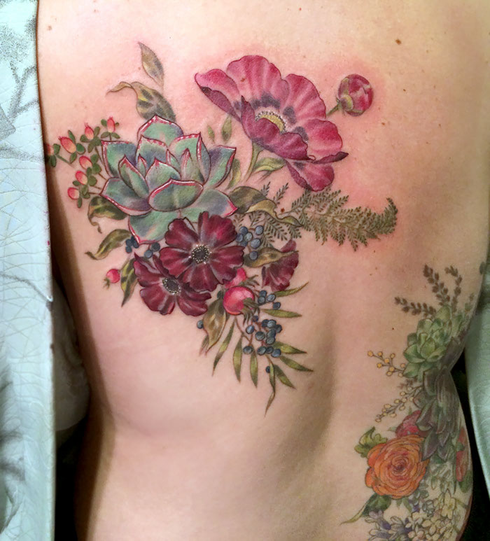 Colorful succulent tattoo design featuring flowers and greenery on a person's back.