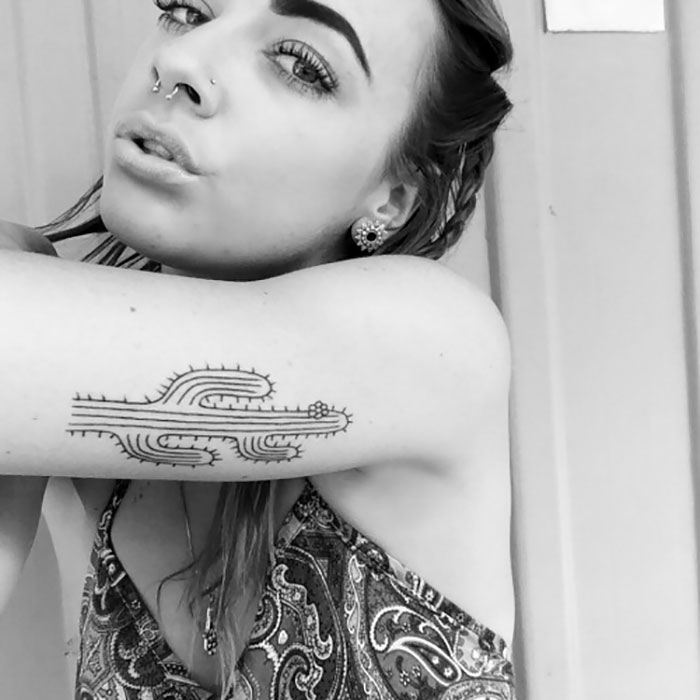 Woman showcasing a succulent tattoo on her forearm, with intricate cactus design.