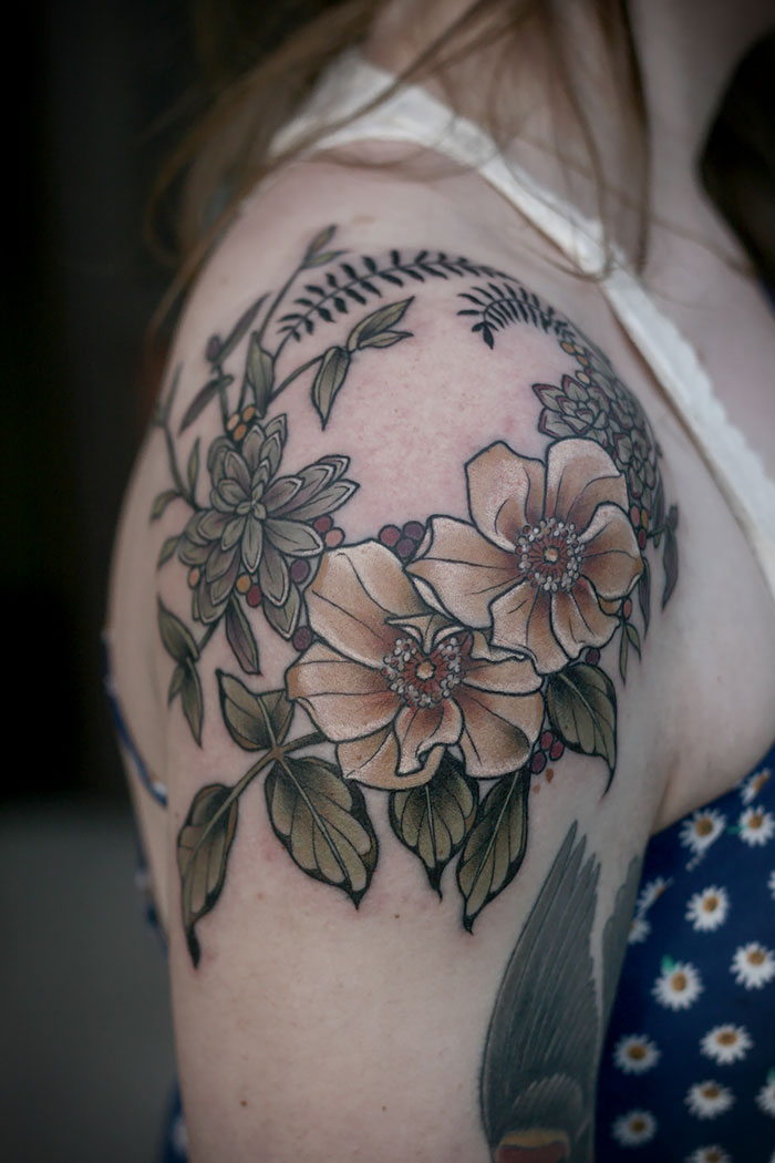 Floral and succulent tattoo on a person's shoulder, featuring detailed greenery and flowers.