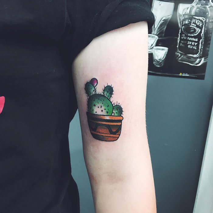 Colorful succulent tattoo of a potted cactus on an upper arm, showcasing unique design for succulent enthusiasts.