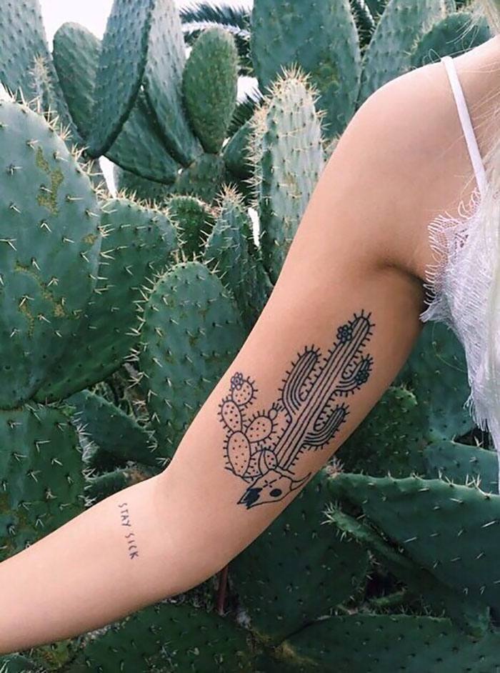 Succulent tattoo design on arm, featuring cacti, surrounded by real succulent plants.