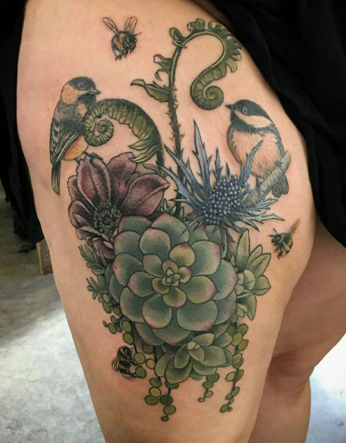 Colorful succulent tattoo featuring birds, bees, and various plants on a person's leg.
