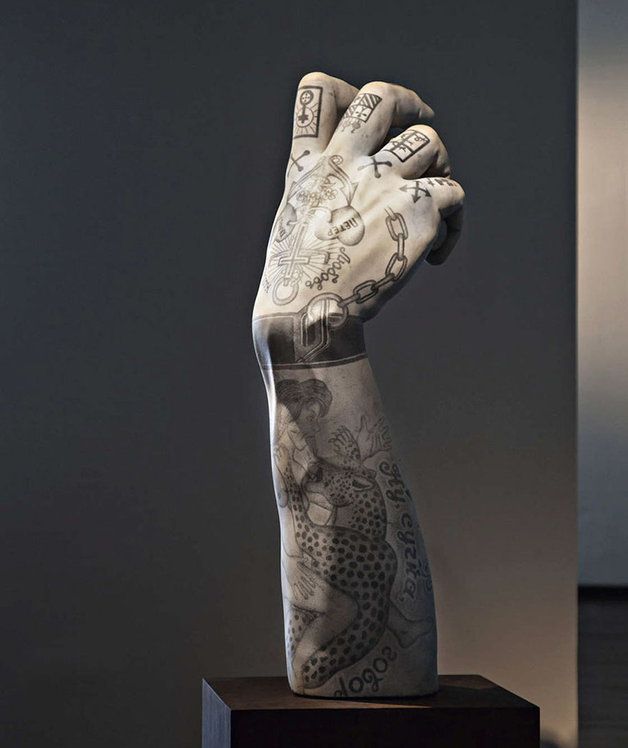 Classical sculpture arm with criminal tattoos by Italian artist, showcased in a modern setting.