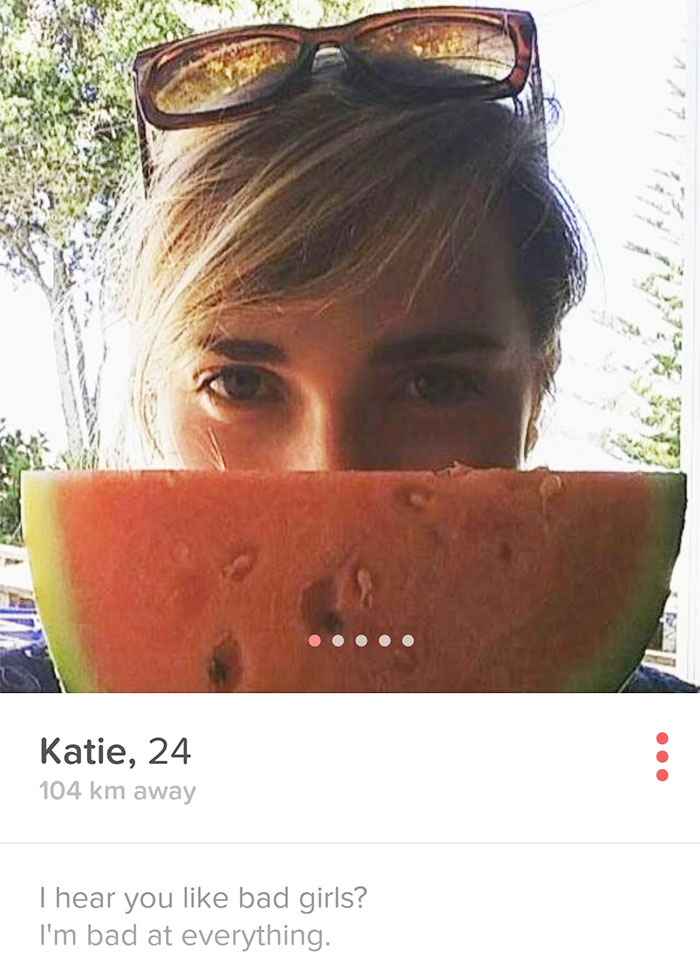 A person humorously hiding behind a slice of watermelon with sunglasses perched on their head, embodying a funny Tinder profile.