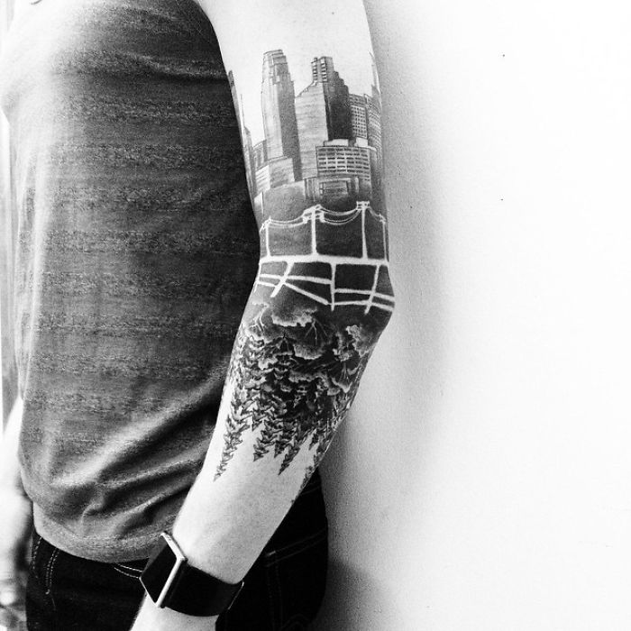Arm with architecture tattoo featuring cityscape and trees, showcasing intricate ink designs.