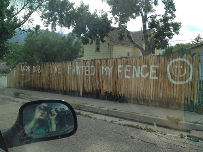 Neighbor's fence with playful painted message: "Look Bob, I've painted my fence" with smiley face, adding humor.