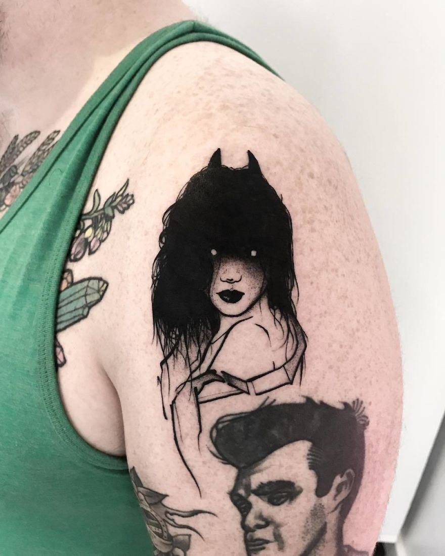 Tattoo of a faceless woman with dark hair and horns on a person's upper arm.