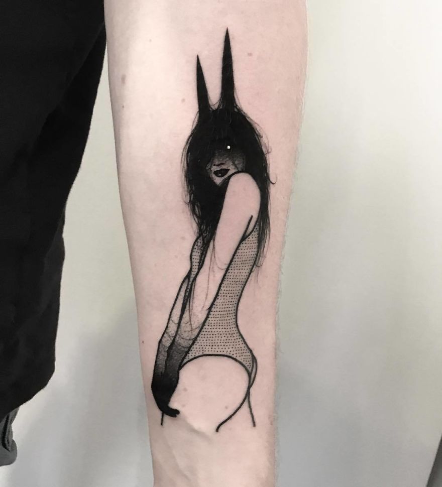 Tattoo of a faceless girl in an artistic pose with bunny ears, slightly erotic design on a person's forearm.