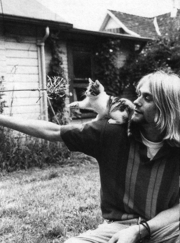 Black and white photo of a famous person playing with a cat perched on their shoulder outdoors, showcasing famous people and their cats.