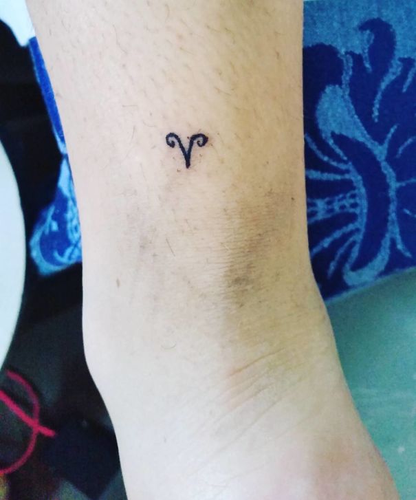 Small tattoo drawn by Brazilian tattoo artist on a person's ankle, featuring a simple Aries symbol.