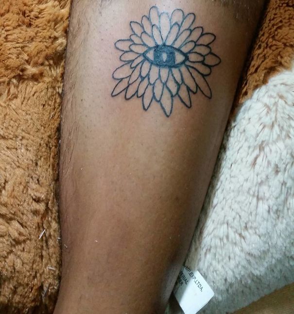 Tattoo of a simple eye within petals on a person's leg, by Brazilian tattoo artist known for unique designs.