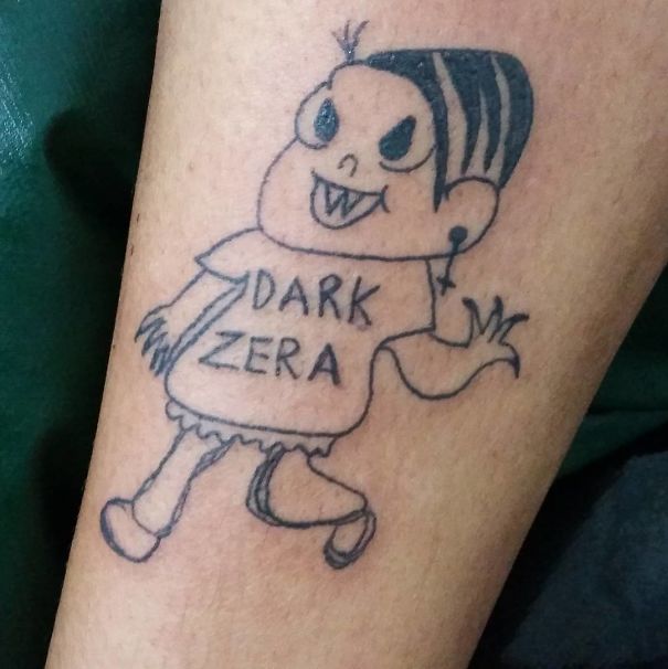 Tattoo of cartoon character with jagged teeth on arm, wearing a shirt labeled "Dark Zera," by Brazilian tattoo artist.