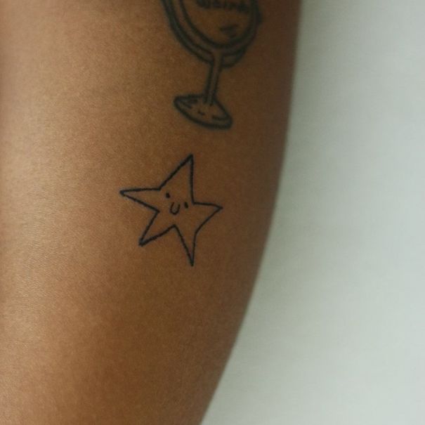 Simple star tattoo with a smiling face on an arm, created by a Brazilian tattoo artist.