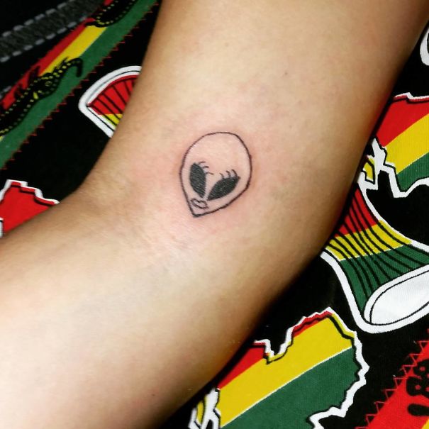 Simple alien tattoo by Brazilian artist on forearm with colorful background.
