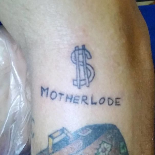 Tattoo of dollar symbol above the word "Motherlode" on skin, created by a Brazilian tattoo artist.