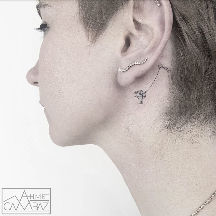 Simple tattoo of a person flying a kite behind the ear by a former Turkish cartoonist.