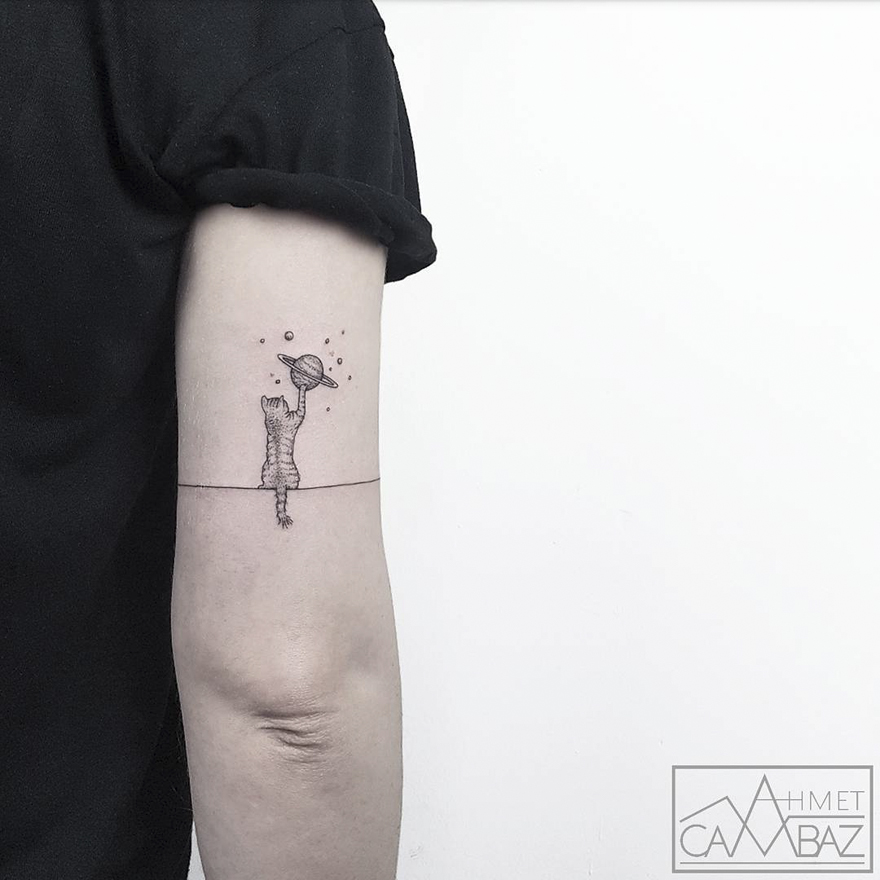 Simple yet striking tattoo of a cat reaching for a planet on a person's arm, designed by a Turkish cartoonist.