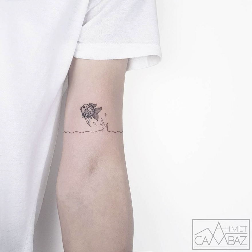 Minimalist fish tattoo by Turkish cartoonist on arm, featuring a fish jumping over a line resembling water.
