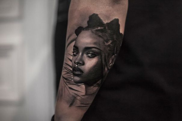 Realistic tattoo by Belgian artist, depicting a woman's face, giving a printed-on-skin impression on an arm.