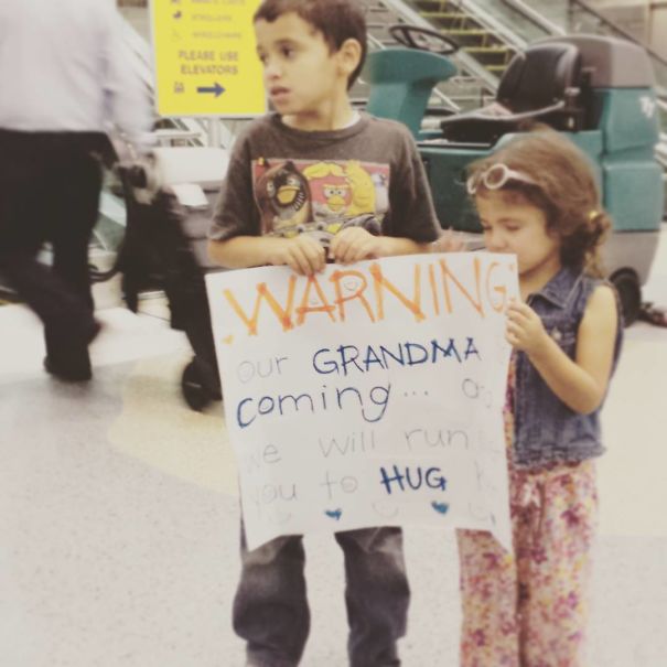 Two kids at airport with a funny sign for grandma, adding humor to the pickup experience.