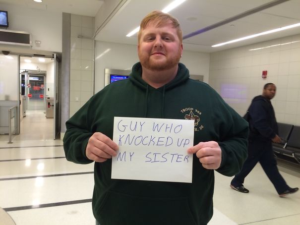 Man holding a funny airport pickup sign with handwritten message in terminal.