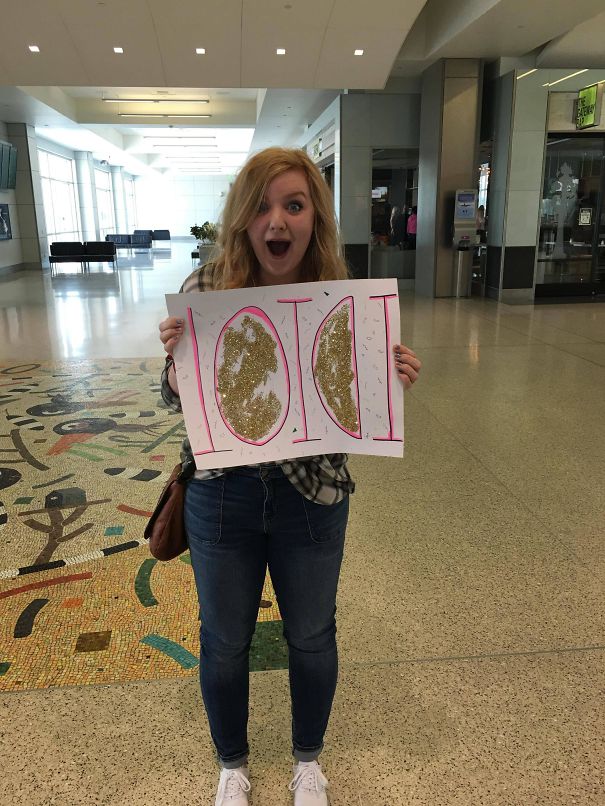 Young woman holding a funny airport pickup sign made of gold glitter letters.