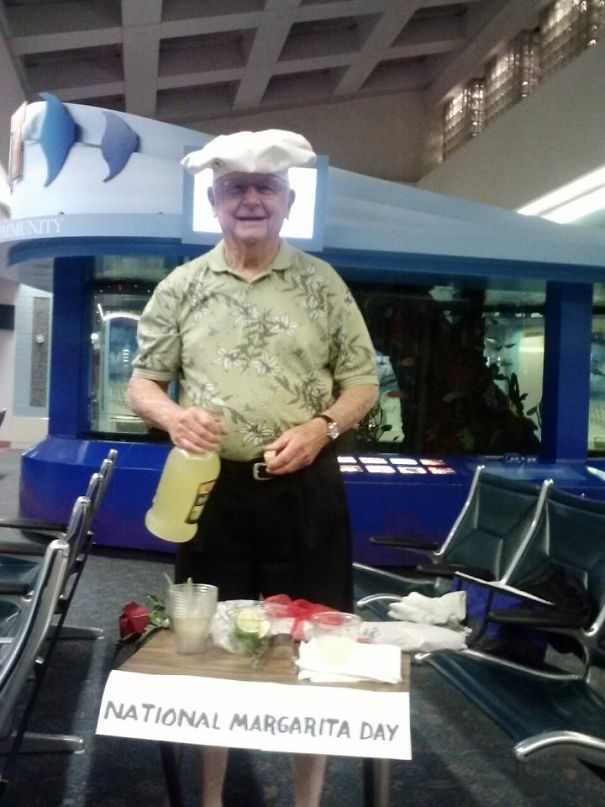 Elderly man holding margarita mix with a humorous airport pickup sign for National Margarita Day.