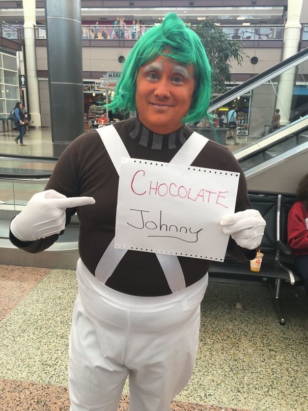Person in costume holding comical airport pickup sign reading "Chocolate Johnny".