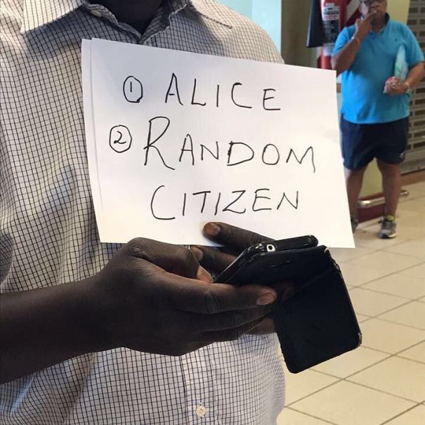 Man holding a funny airport pickup sign that reads "1. Alice 2. Random Citizen" while using a phone.