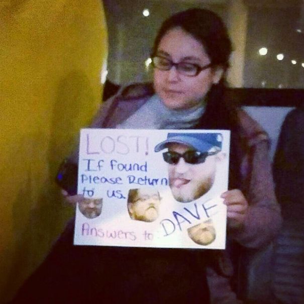Woman holding a funny airport pickup sign with photos and text asking to return "Dave."