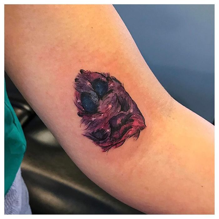 Dog paw print tattoo on an arm, featuring detailed colors and shading.