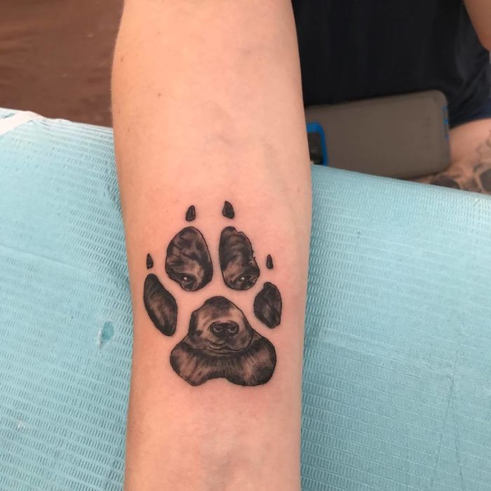 Dog paw print tattoo with a dog's face, showcasing creative ink design on a forearm.